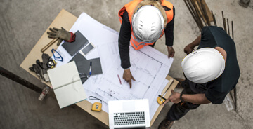Two men discussing blue prints at a job site wearing white hard hats